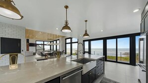 Une cuisine moderne dotée d’un grand îlot central, d’appareils électroménagers en acier inoxydable et de luminaires suspendus.