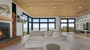 Un salon moderne doté d’une cheminée, de grandes fenêtres et offrant une vue sur l’océan.