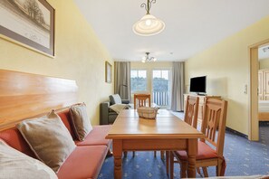 Une pièce comprenant une table à manger en bois, des chaises, un canapé, un téléviseur et une grande fenêtre donnant sur un beau paysage.
