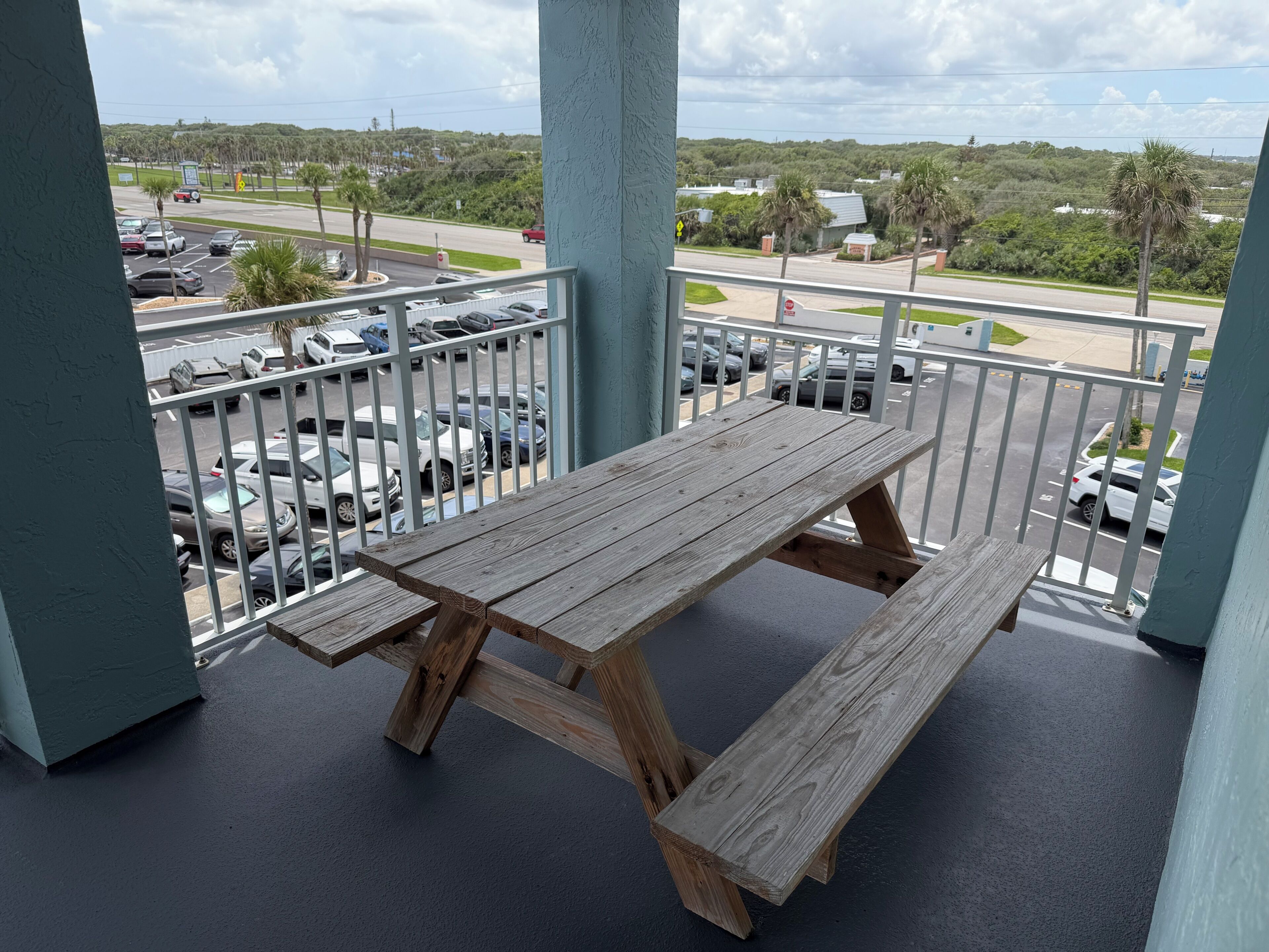 Une table de pique-nique en bois sur un balcon, avec vue sur un parking et une route.