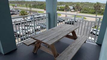 Une table de pique-nique en bois sur un balcon, avec vue sur un parking et une route.