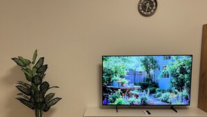 Et fjernsyn på et hvidt stativ med en potteplante ved siden af.