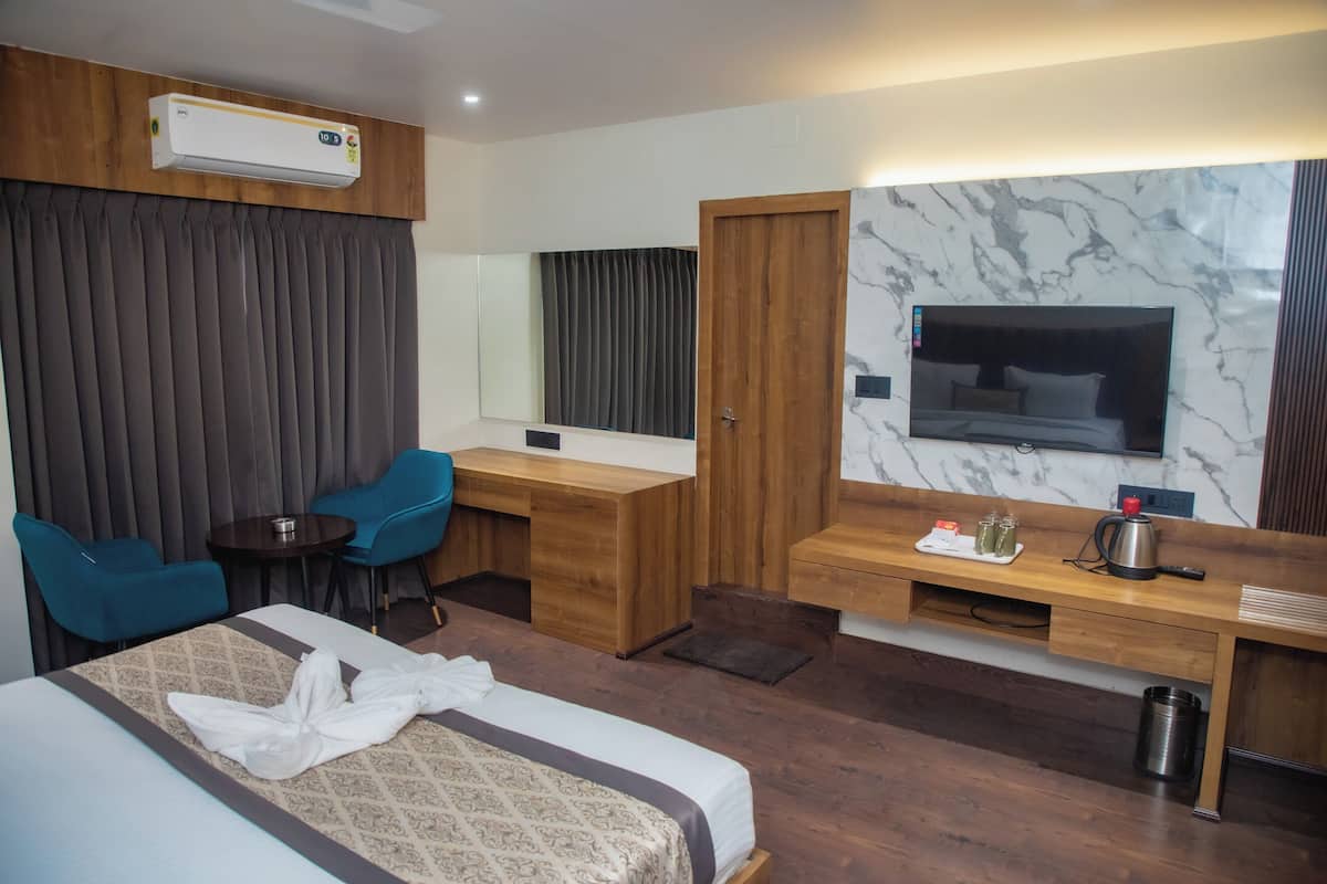 Una habitación de hotel con una cama, un escritorio, dos sillas, un espejo y un televisor.