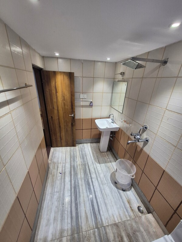 A bathroom with a marble floor, a sink, a mirror, and a shower. - Hotel Centrum (Siliguri)