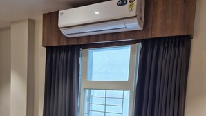 Ein Zimmer mit zwei blauen Stühlen, einem runden Tisch, einem Fenster mit Jalousien und einer Klimaanlage darüber.