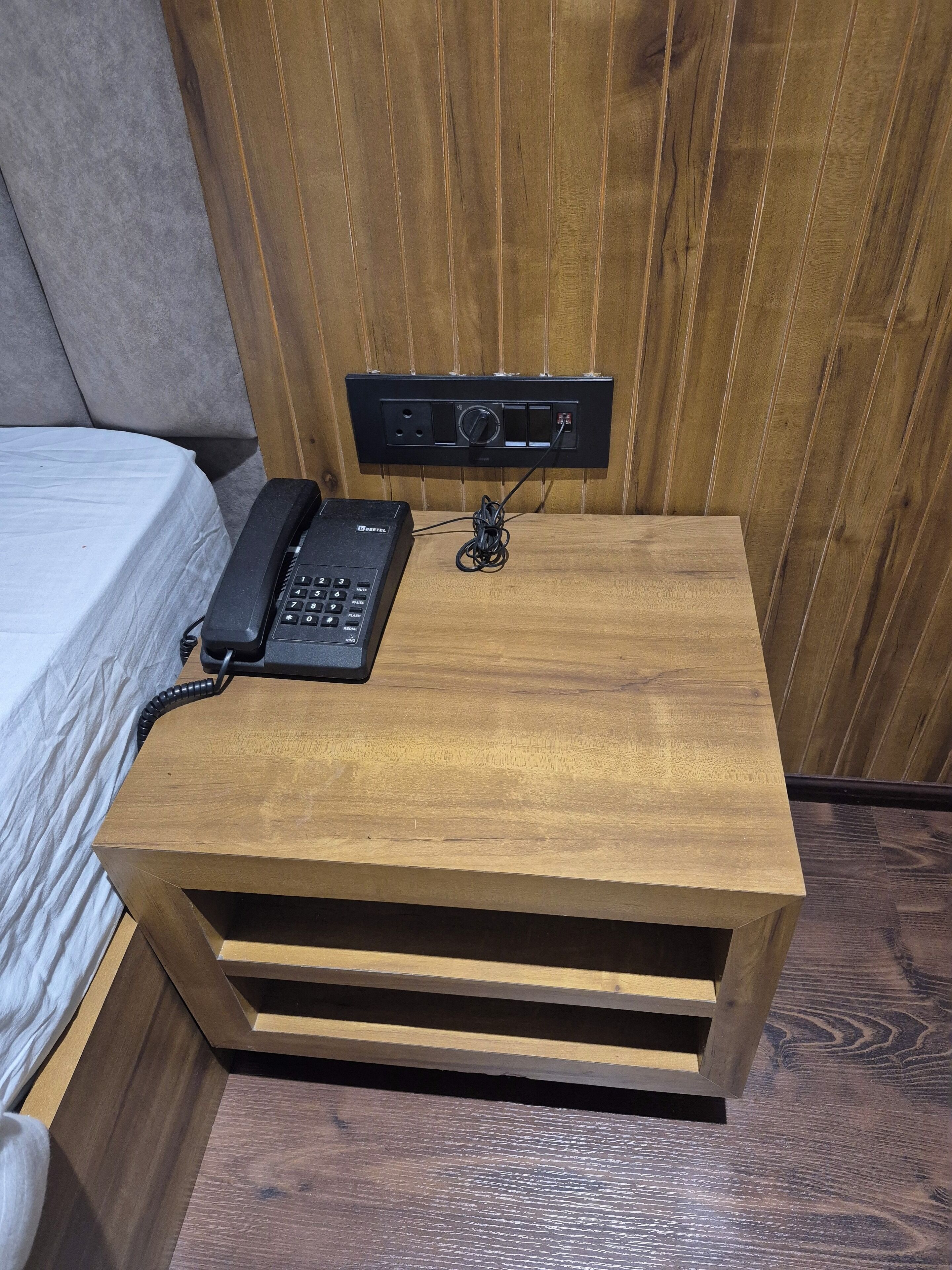 A wooden bedside table with a telephone and a power strip.