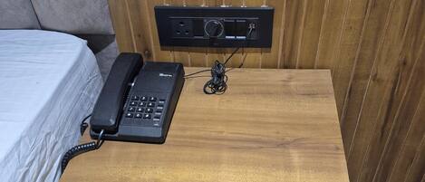 A wooden bedside table with a telephone and a power strip.
