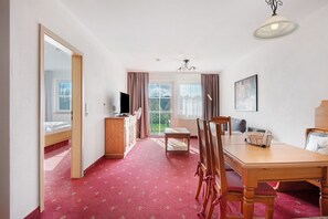 A room with a wooden dining table, chairs, a television, a cabinet, and a window with curtains. - Superior Apartment with Lake View K2 102 (Spalt)