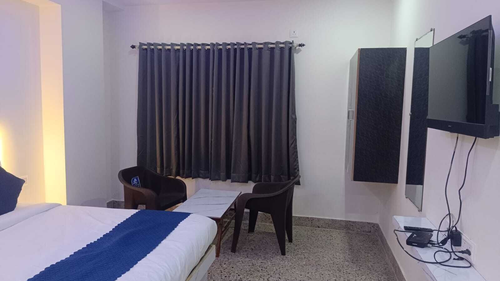 A hotel room with a bed, two chairs, a desk, a TV, and a curtain.