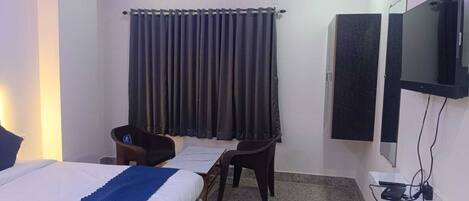 A hotel room with a bed, two chairs, a desk, a TV, and a curtain.