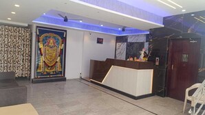 A reception area with a marble floor, a reception desk, a wall-mounted clock, and a decorative mural. - HOTEL JAGAPATHI INTERNATIONAL (Vijayawada)