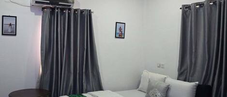 Une chambre à coucher avec un lit, une petite table, un appareil de climatisation et des rideaux gris.
