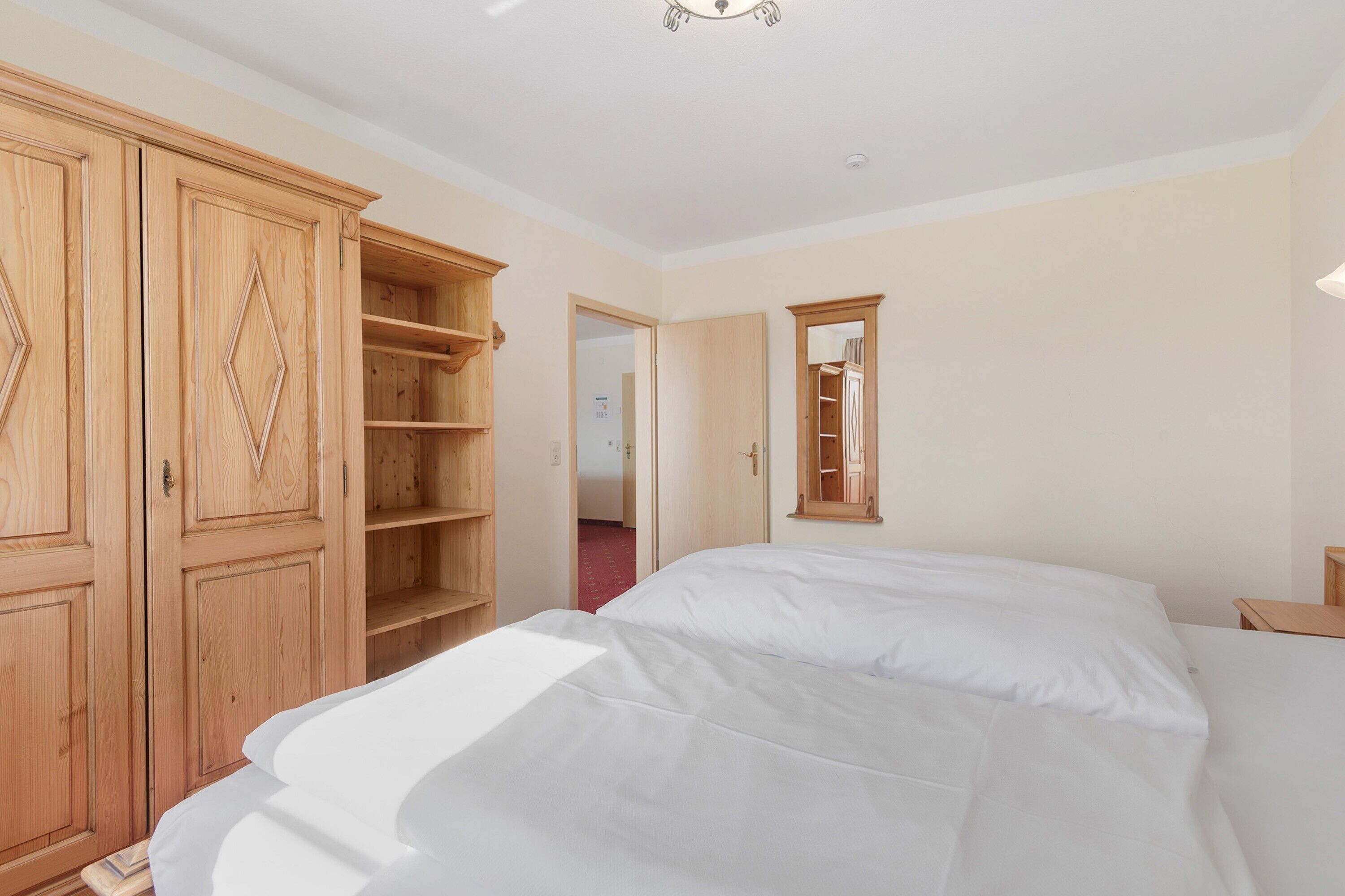 A bedroom with a bed, wooden wardrobe, and a mirror.