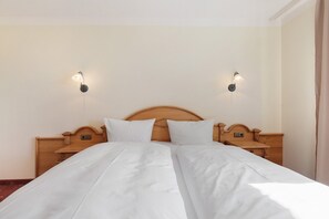 Un lit double avec une literie blanche, une tête de lit en bois, des tables de chevet et des lampes fixées au mur.