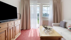 Una habitación con una televisión sobre un mueble de madera, un sofá con cojines, una mesa con un cuenco decorativo y vistas a través de una puerta de cristal.