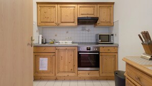 Una cocina con armarios de madera, microondas, horno y un cubo de basura.