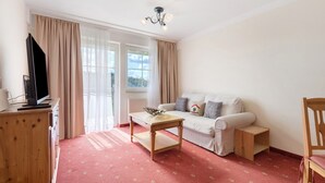 Una sala de estar con un sofá, una mesa de centro de madera, un televisor sobre un mueble de madera y una ventana con cortinas.