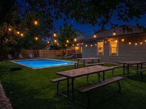 Ein Garten mit Swimmingpool, Picknicktischen und Lichterketten.
