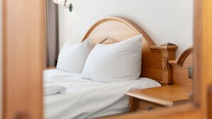 A neatly made bed with white linens and pillows, a wooden headboard, and a bedside table with a lamp.