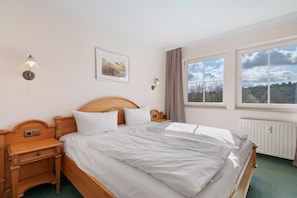 Een slaapkamer met een houten bed, nachtkastjes, een wandlamp en een foto in een lijst, plus een raam met uitzicht.