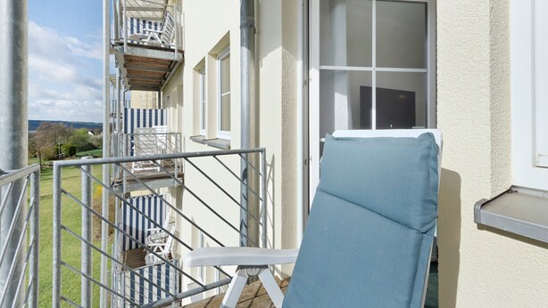 A balcony with a blue chair, a metal staircase, and a window.