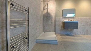 A modern bathroom with a walk-in shower, a glass-enclosed toilet, and a vanity with a mirror.