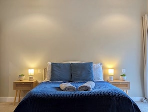 A neatly made bed with a blue blanket and two pillows, flanked by bedside tables with lamps and small potted plants.