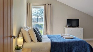 A bedroom with a bed, a TV, a nightstand, a window with curtains, and a lamp.