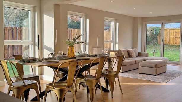 A spacious dining area with a wooden table and chairs, a sofa, and a view of the backyard through large windows.