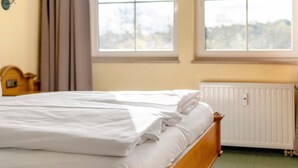 A neatly made bed with white linens in a room with two windows and a radiator. - Deluxe Apartment with Lake View K3 003 (Spalt)