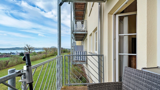 A balcony with a metal railing, a wicker sofa, and a view of the countryside. - Deluxe Apartment with Lake View K3 003 (Spalt)
