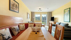 A room with a wooden dining table, a sofa with patterned cushions, a television, and a painting on the wall. - Deluxe Apartment with Lake View K3 003 (Spalt)