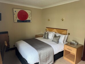 A hotel room with a large bed, two bedside tables, a nightstand, a wall-mounted artwork, and a wooden headboard.