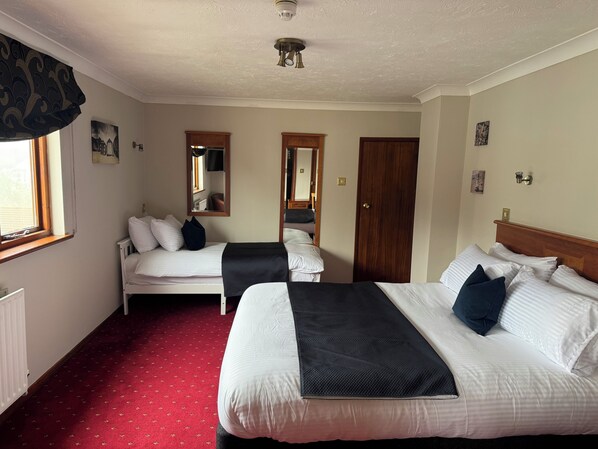 A hotel room with two beds, a red carpet, a ceiling fan, and a window with curtains. - The Windsor House Hotel (Worthing)
