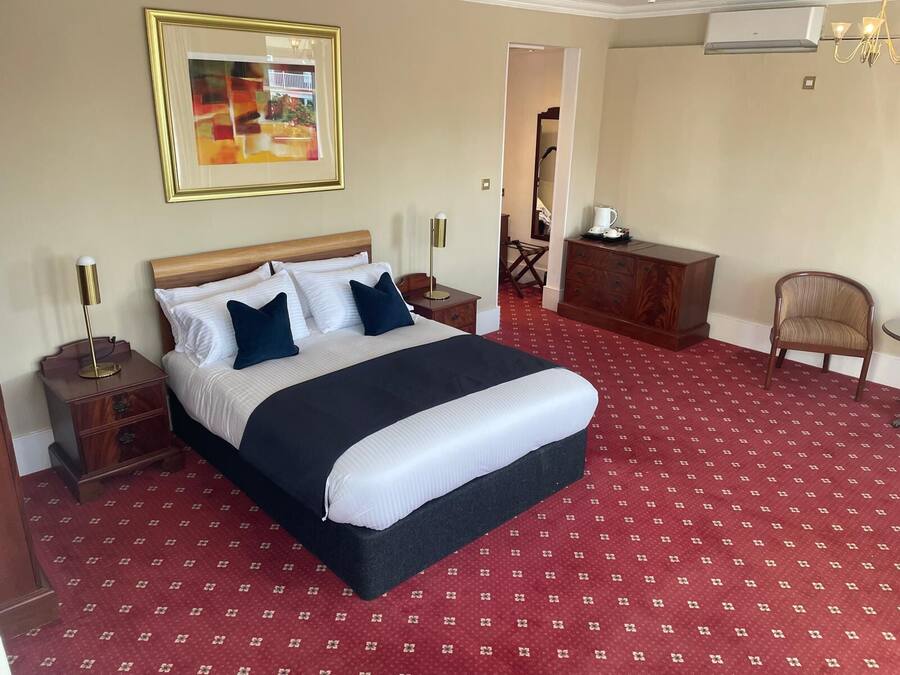 Une chambre d’hôtel avec un grand lit, une table de chevet, une commode, une chaise et un tableau au mur.