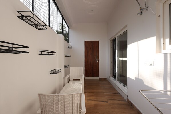 Un couloir étroit avec un plancher en bois, un mur blanc orné d’étagères noires, une chaise en osier blanche et une porte en bois au fond.