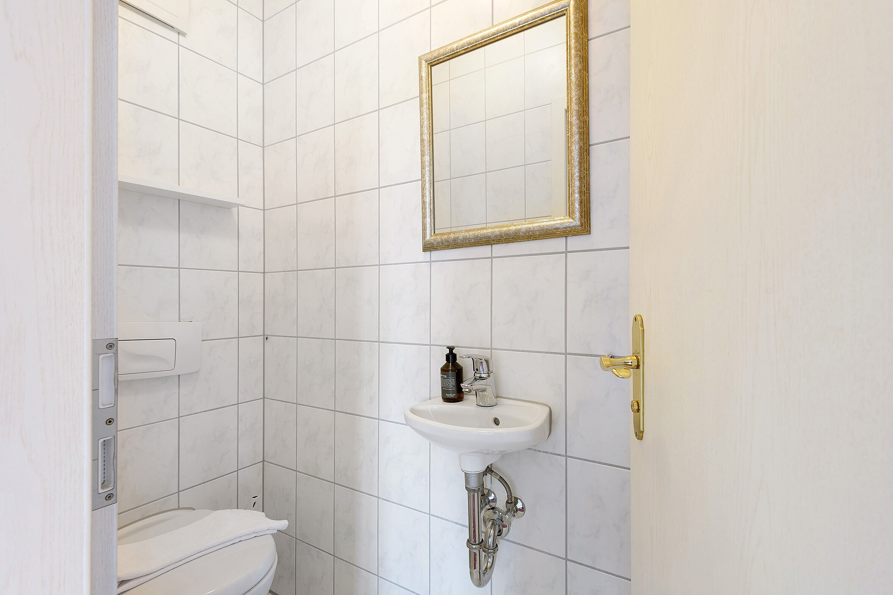 A bathroom with a white tiled wall, a white sink with a gold frame mirror, and a toilet.