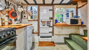 Cocina compacta con estufa, horno y microondas. Hay ollas y sartenes colgando, y una ventana que proporciona luz natural.