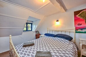A bedroom with a sloped ceiling, a bed with patterned bedding, a nightstand, and a wall-mounted light fixture. - Old Town Cottage, Hastings (Hastings)