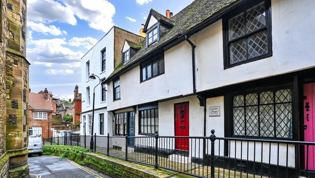 Una calle estrecha con edificios tradicionales, incluyendo un edificio blanco con puerta roja y un letrero que dice "Farmer's House".