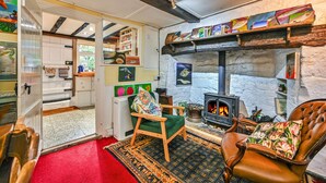 Una habitación acogedora con chimenea, una silla verde, un sillón de cuero y una estantería con obras de arte.