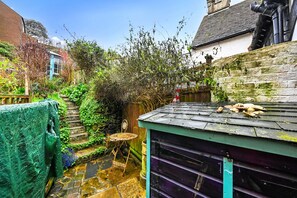 A narrow garden with a wooden table and chairs, a small shed, and a stone pathway. - Old Town Cottage, Hastings (Hastings)