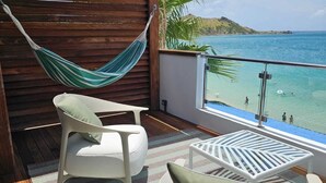 Un balcone con un'amaca, due sedie bianche, un tappeto decorato e vista sul mare e un'isola in lontananza.