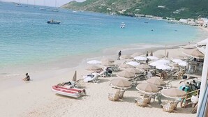 Una spiaggia con lettini e ombrelloni, una barca sull'acqua e un paesaggio collinare sullo sfondo.