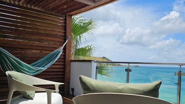 Un balcone con due sedie bianche, un'amaca verde e vista sull'oceano.