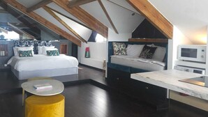 Una moderna camera da letto mansardata con travi a vista in legno, un letto grande, un letto più piccolo, un'area pranzo e una cucina.
