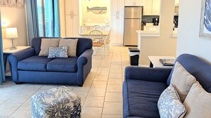 Uma sala de estar com sofá, um banquinho e uma área de jantar com cadeiras e mesa.