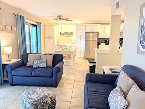 A living room with a sofa, ottoman, and a dining area with chairs and a table. - 2 BR Ocean View Condo | Myrtle Beach Resort B0316 (Myrtle Beach)