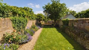 A garden with a stone wall, a grassy lawn, and flowering plants. - Cosy Cottage in Moreton-in-Marsh (Gloucestershire)