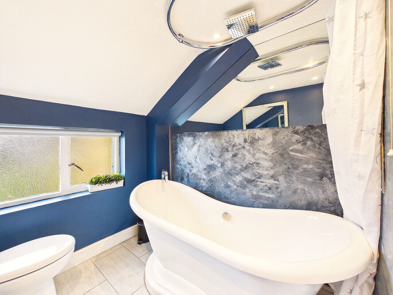 Een badkamer met een vrijstaand bad, toilet, raam met uitzicht en een douchegedeelte.